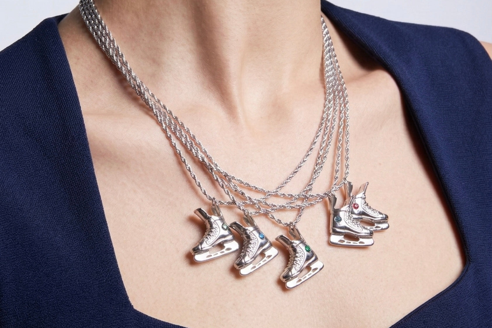 Silver necklaces with ice skate pendants on a person wearing a navy blue top.